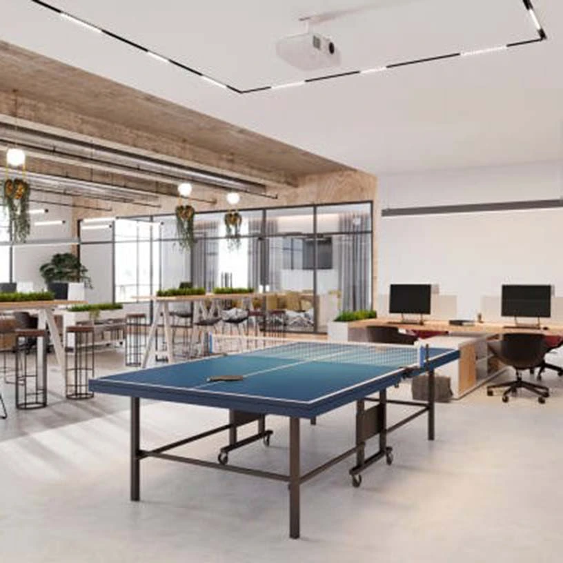 Bureau moderne et spacieux avec table de ping-pong au centre, postes de travail et espaces de détente en arrière-plan.