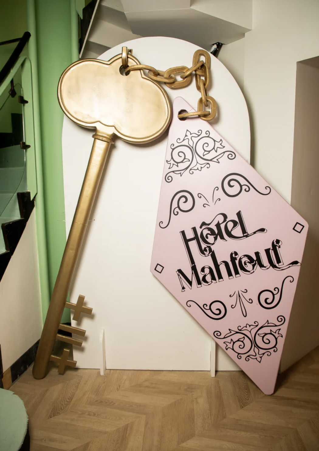 Clé dorée géante avec porte-clés rose ‘Hôtel Mahfouf’, décor au style vintage.