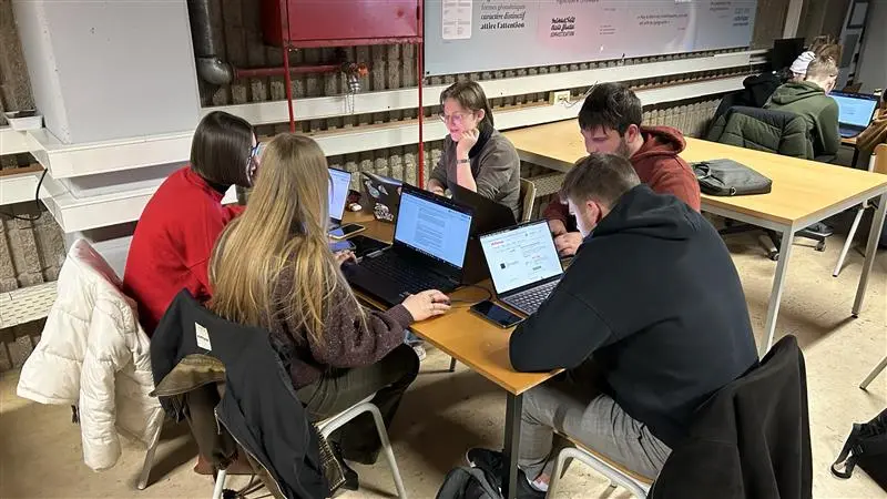 Groupe de jeunes adultes collaborant autour de plusieurs ordinateurs portables dans un environnement de travail partagé.