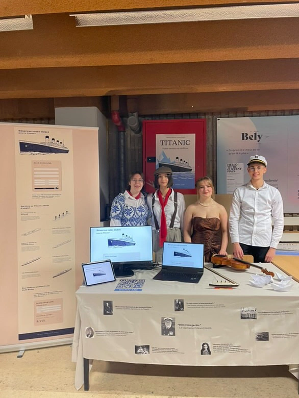 Photo d’un stand de présentation sur le Titanic avec quatre personnes costumées devant des affiches, ordinateurs, violon et documents.